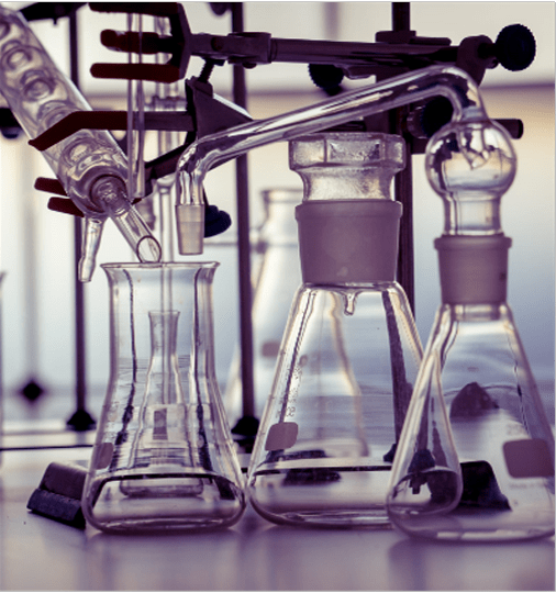 Laboratory glassware on a table, including flasks, beakers, and a distillation apparatus.