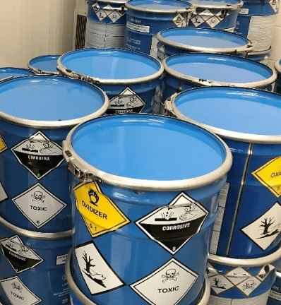 A stack of blue metal barrels, each labeled with hazardous symbols like toxic, corrosive, and oxidizer, indicating danger and caution.