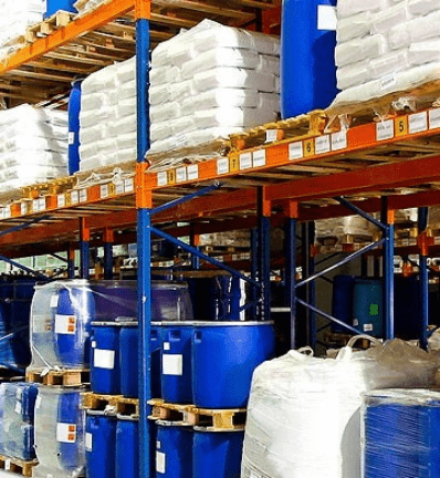 Warehouse shelves filled with stacks of white bags and large blue barrels.
